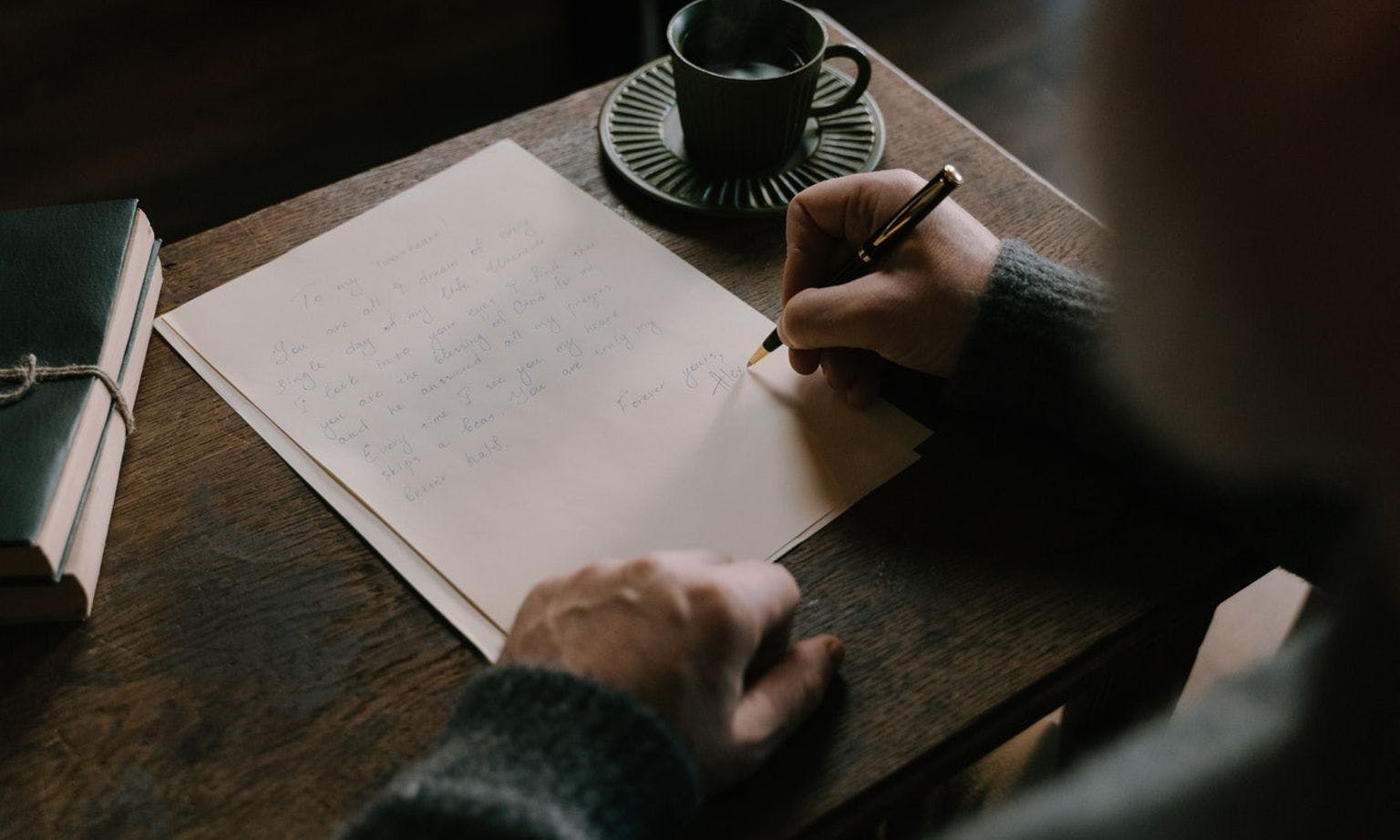 Over the shoulder image of a person writing a letter on an old wooden desk